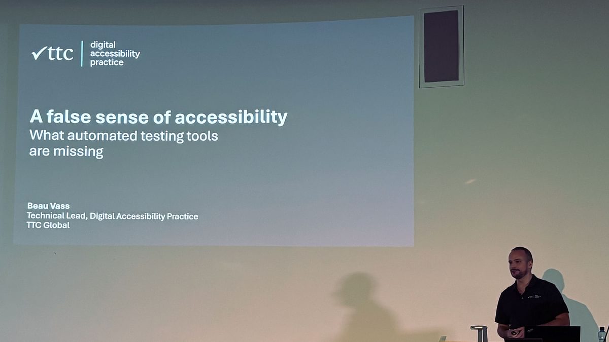 Beau standing at a lecturn presenting. The slide is projected onto the wall it reads A false sense of accessibility testing, what automated testing tools are missing.