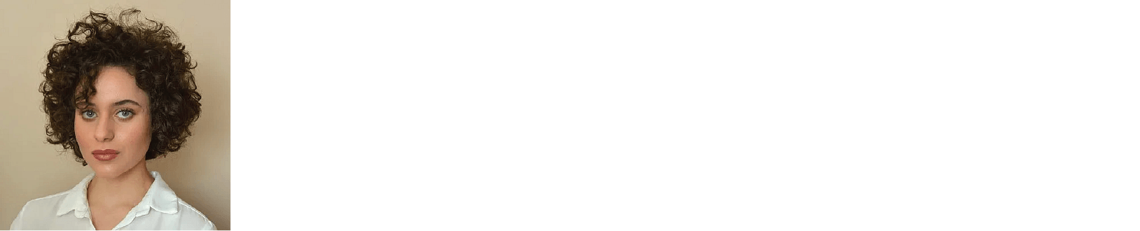 Simone has dark curly hair, blue eyes and is wearing a white shirt.