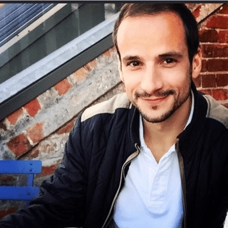 Beau has short dark brown hair, dark brown eyes and trimmed facial hair, an olive complexion, and is wearing a white shirt with a dark jacket, and is smiling.