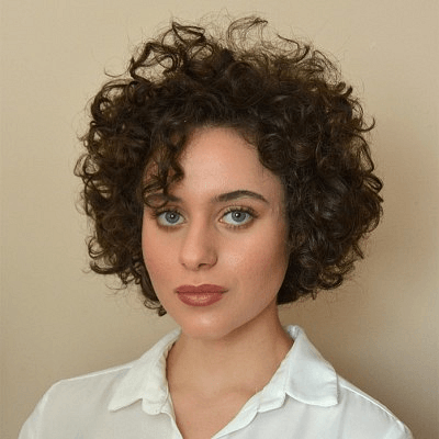Simone has dark curly hair, blue eyes and is wearing a white shirt.