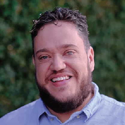 Ben has short brown wavy hair, a brown beard and is wearing a blue shirt