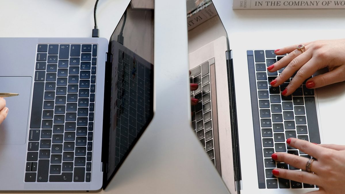 Two laptops facing opposite each other on a work desk with papers, books and stationery neatly placed around them.